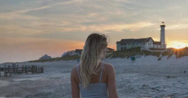 Wind-swept hair at the beach during sunset, with lighthouse in the background.