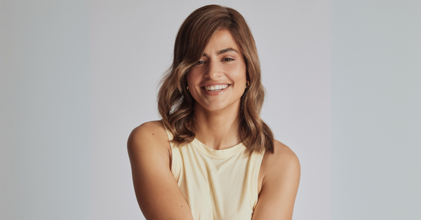 Smiling woman with healthy, hydrated hair styled in soft waves, representing the benefits of glycerin in Unwritten Haircare for moisture and shine.
