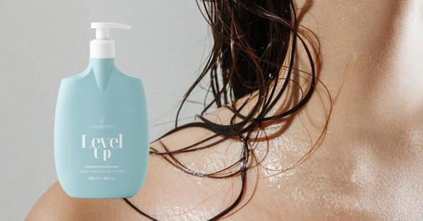 Unwritten Level Up conditioner beside wet hair on a woman's shoulder.