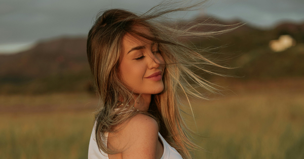 Smiling woman with windswept blonde hair outdoors, representing the hydrating benefits of hydrolyzed hyaluronic acid for healthy, nourished hair.